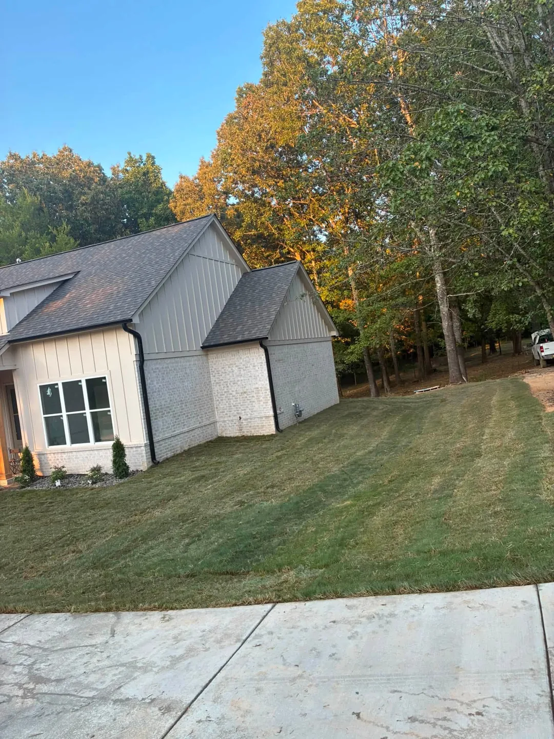 Fresh sod around a home beside a concrete driveway and mature trees