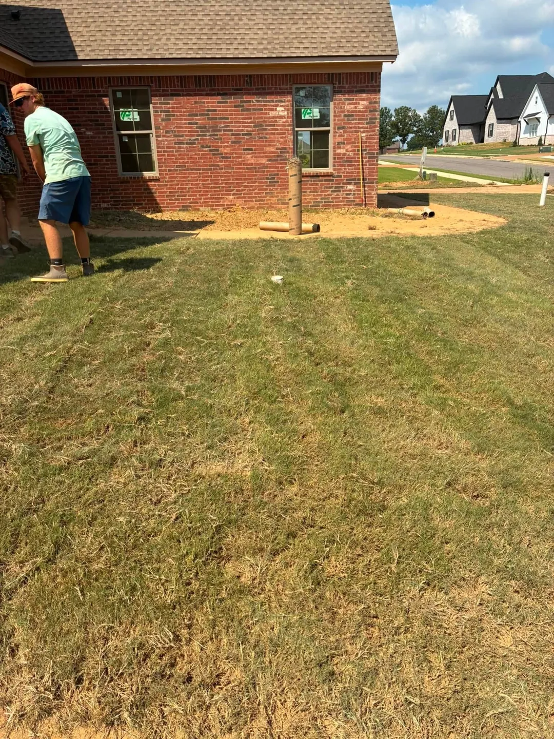 A worker beside newly laid sod and a brick garage